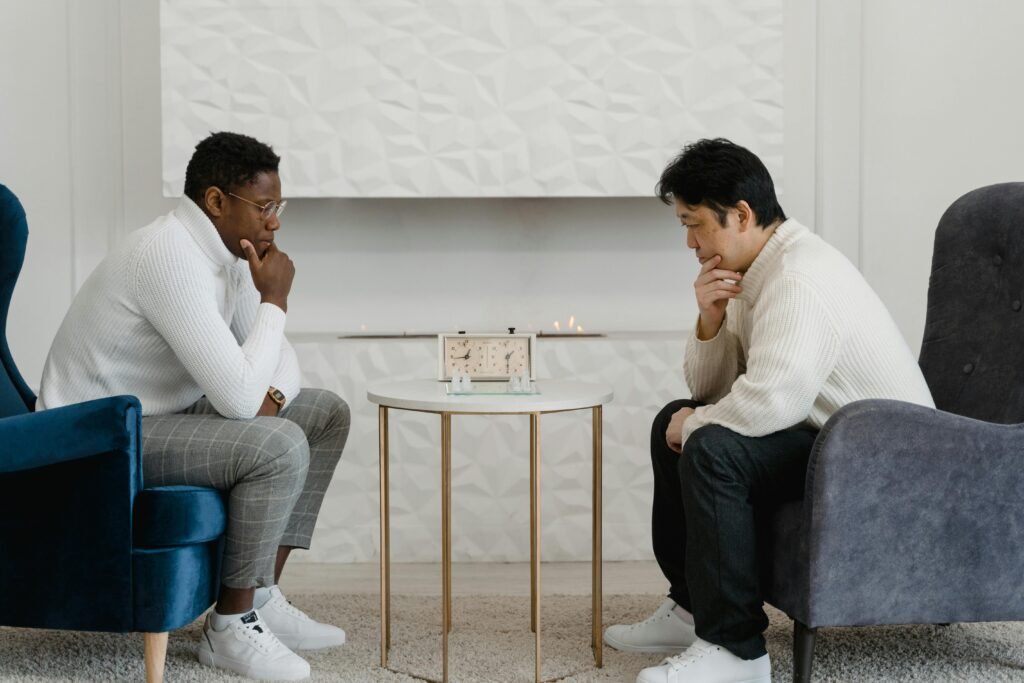 Two men engage in a thoughtful chess game indoors with a chess clock on a round table.