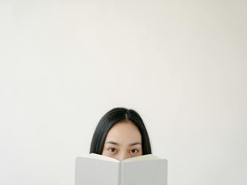 Blank wall with upper part of Asian woman face hidden behind white book