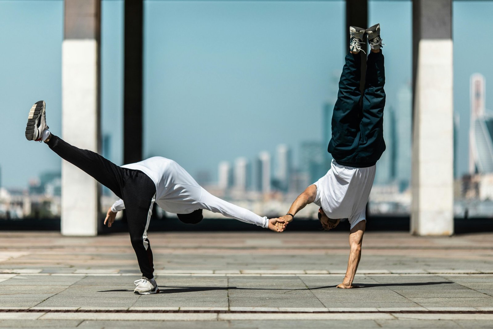 Two dancers perform a dynamic street dance move outdoors, showcasing balance and synchronization.