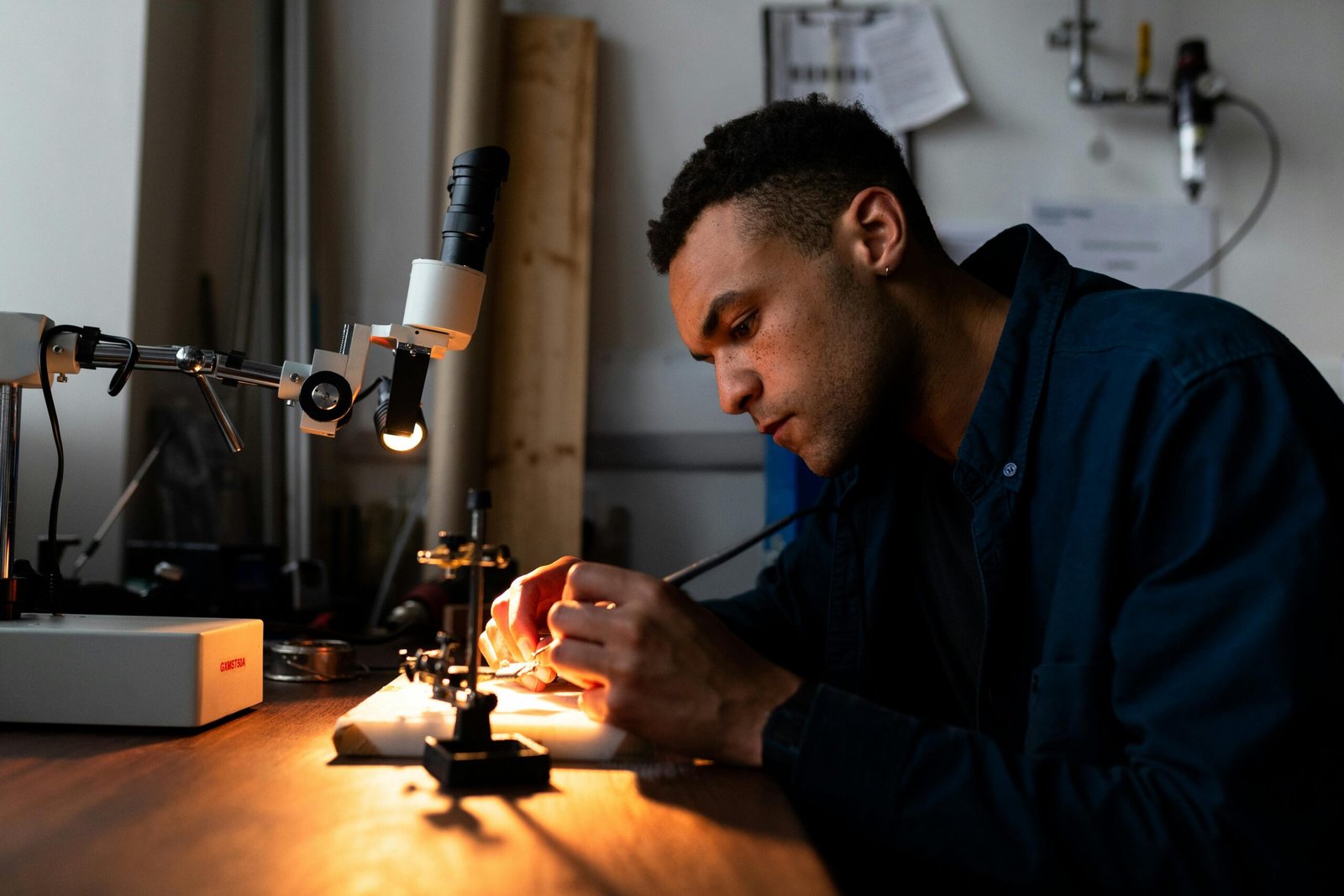 Engineer working with precision tools on electronic components in a well-lit workshop.