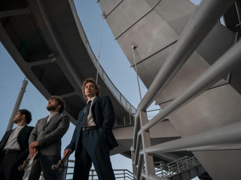 Three young professionals in suits stand confidently beneath a futuristic bridge structure.