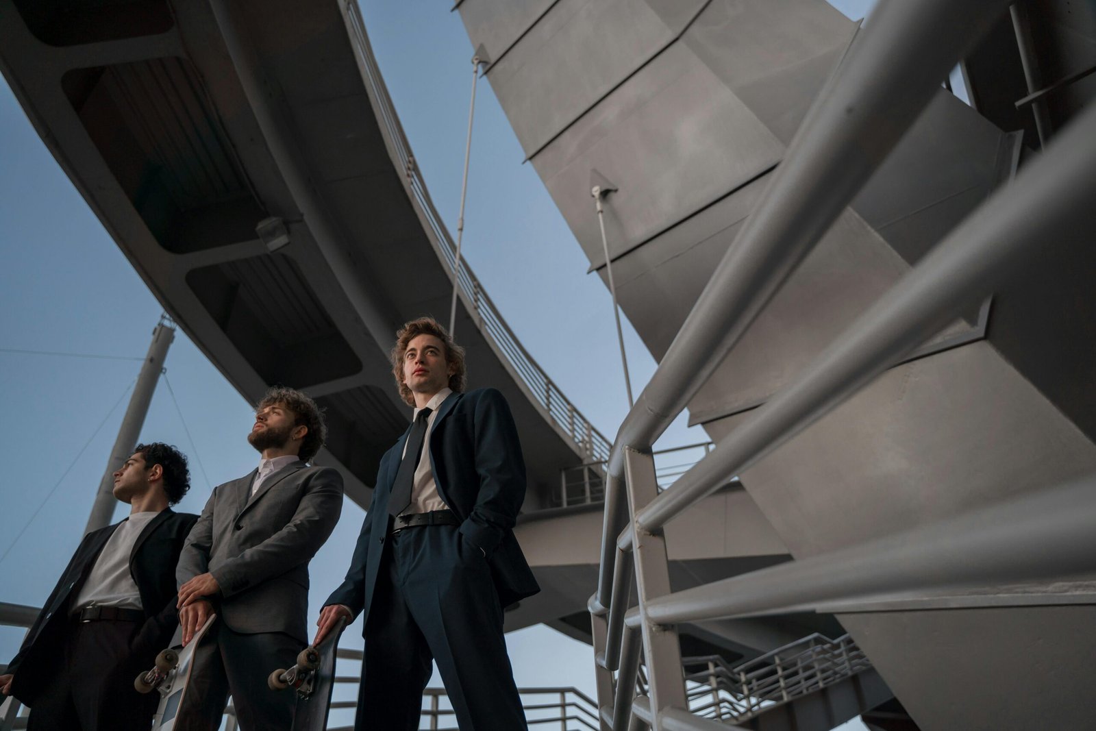 Three young professionals in suits stand confidently beneath a futuristic bridge structure.