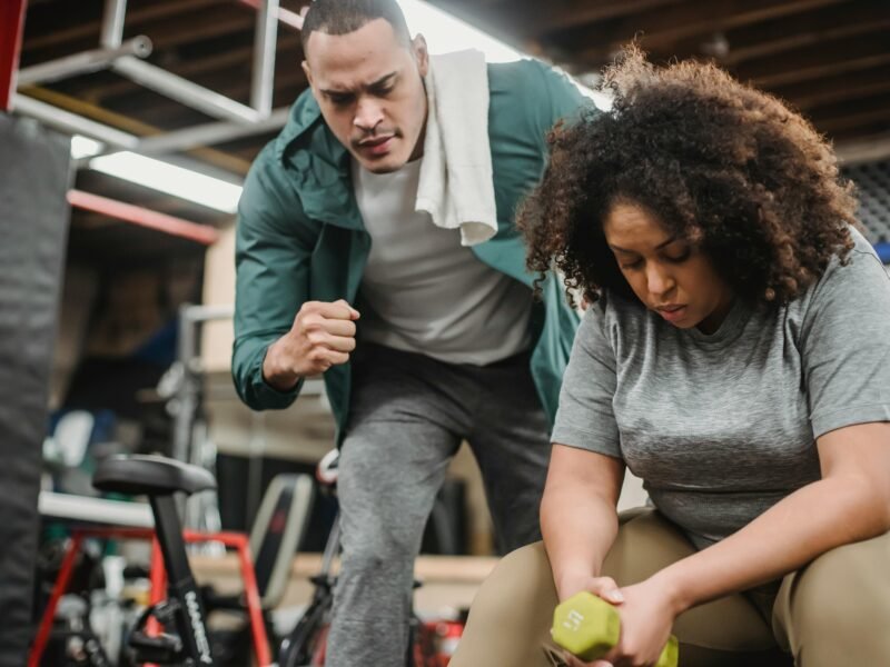 From below of strong personal coach explaining black woman how to exercise with dumbbells properly