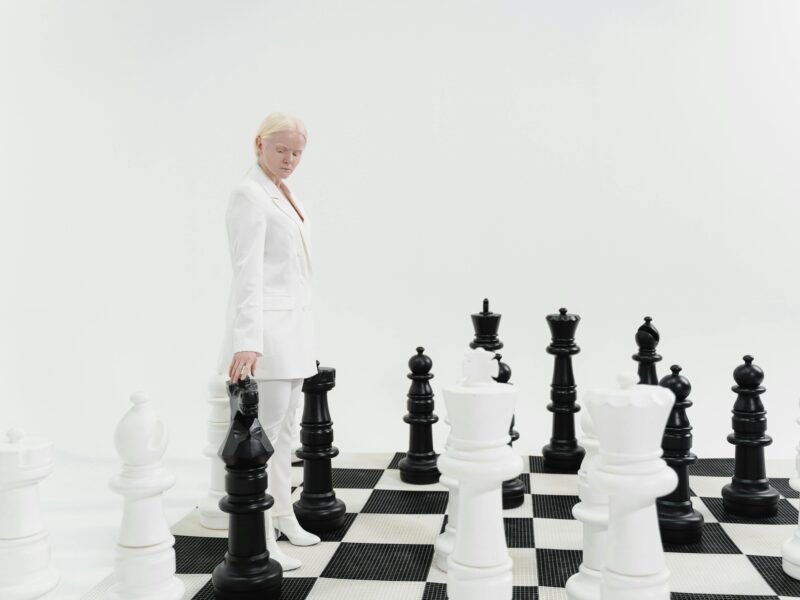 Woman in a white suit strategizing on a giant chessboard indoors.