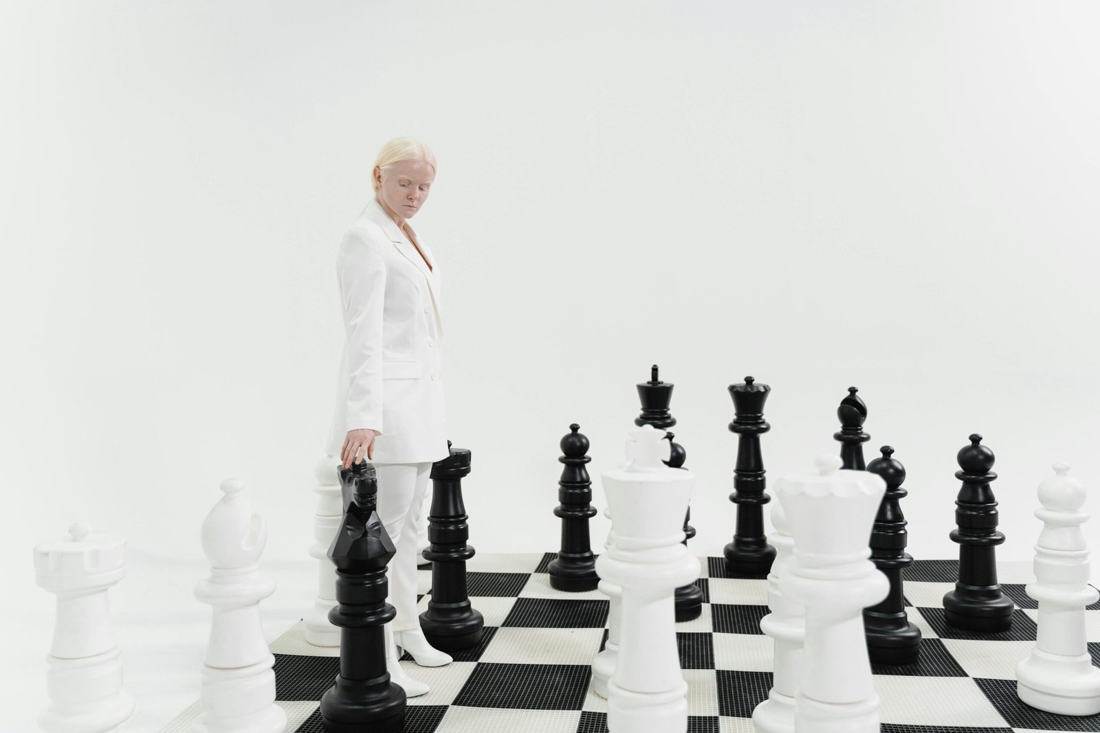 Woman in a white suit strategizing on a giant chessboard indoors.