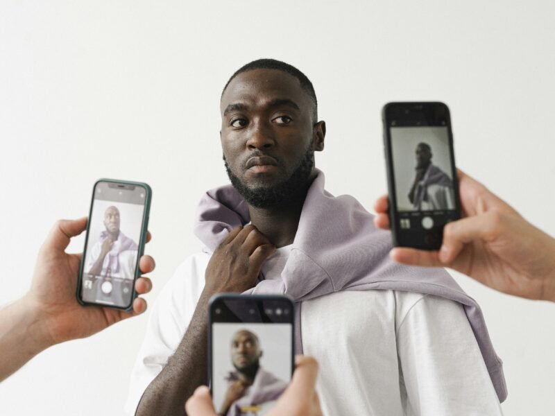 Portrait of a stylish man surrounded by smartphones capturing his image indoors.